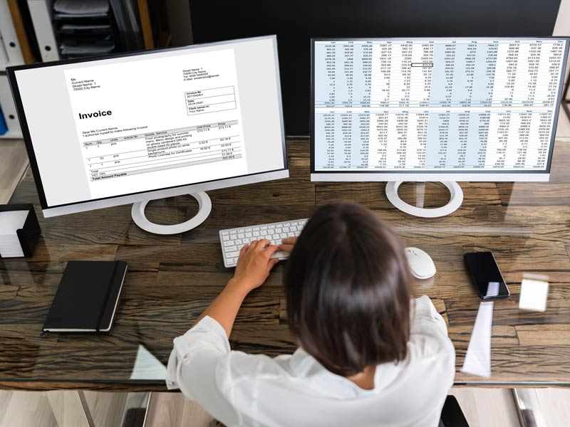 benefits-payment-account-information Person looking a screen with an invoice and another screen with data table