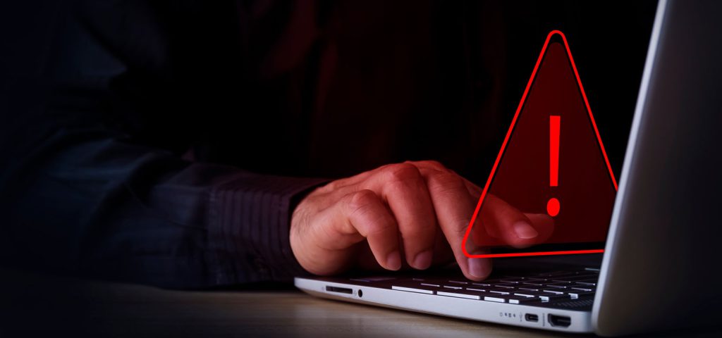 person sitting at a laptop with warning sign