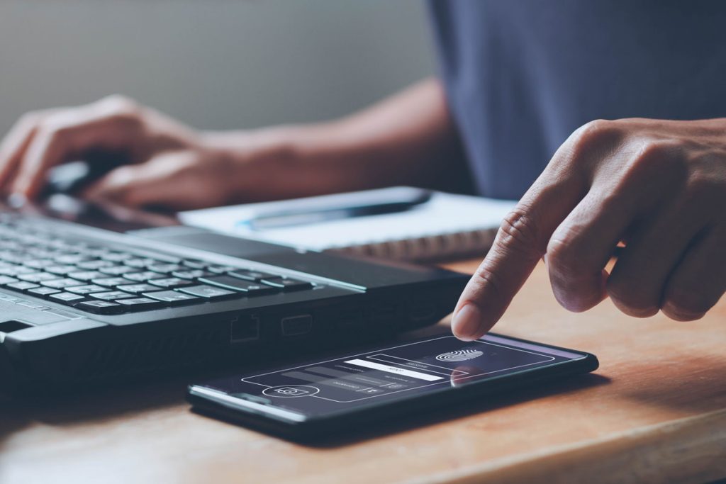 A hand about to tap a phone screen next to a computer.