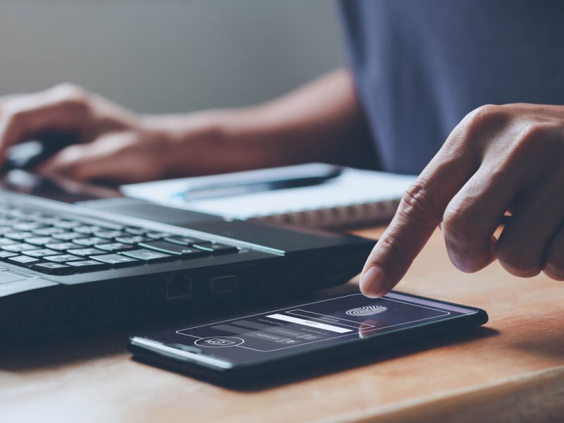 A hand about to tap a phone screen next to a computer.