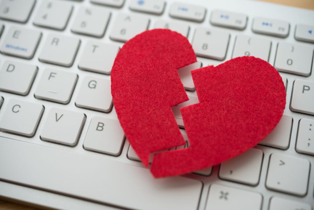 Photo of a red, broken heart on a white computer keyboard.