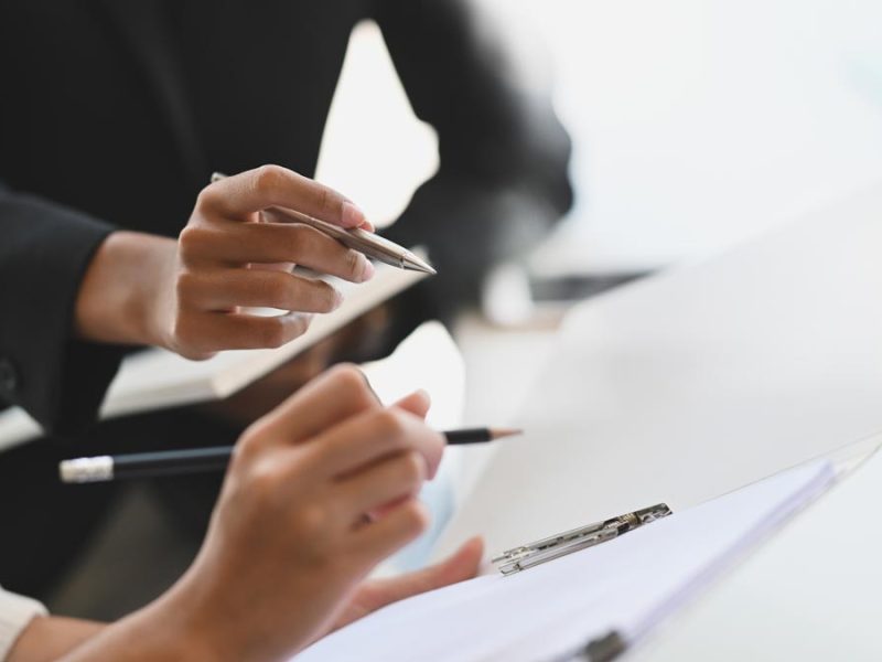 two people holding pens just over a sheet of paper